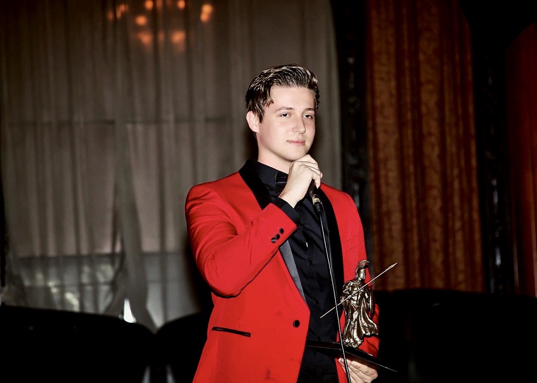 Brian Grajek in a red jacket, speaking and holding an award